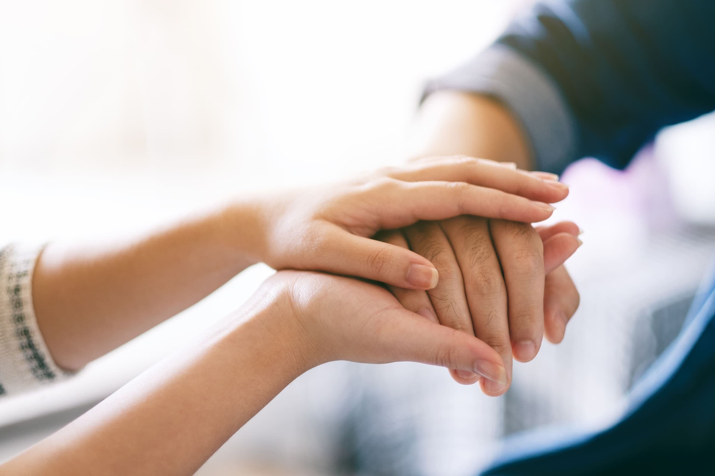 A close-up of two people holding hands, one hand resting on top of the other